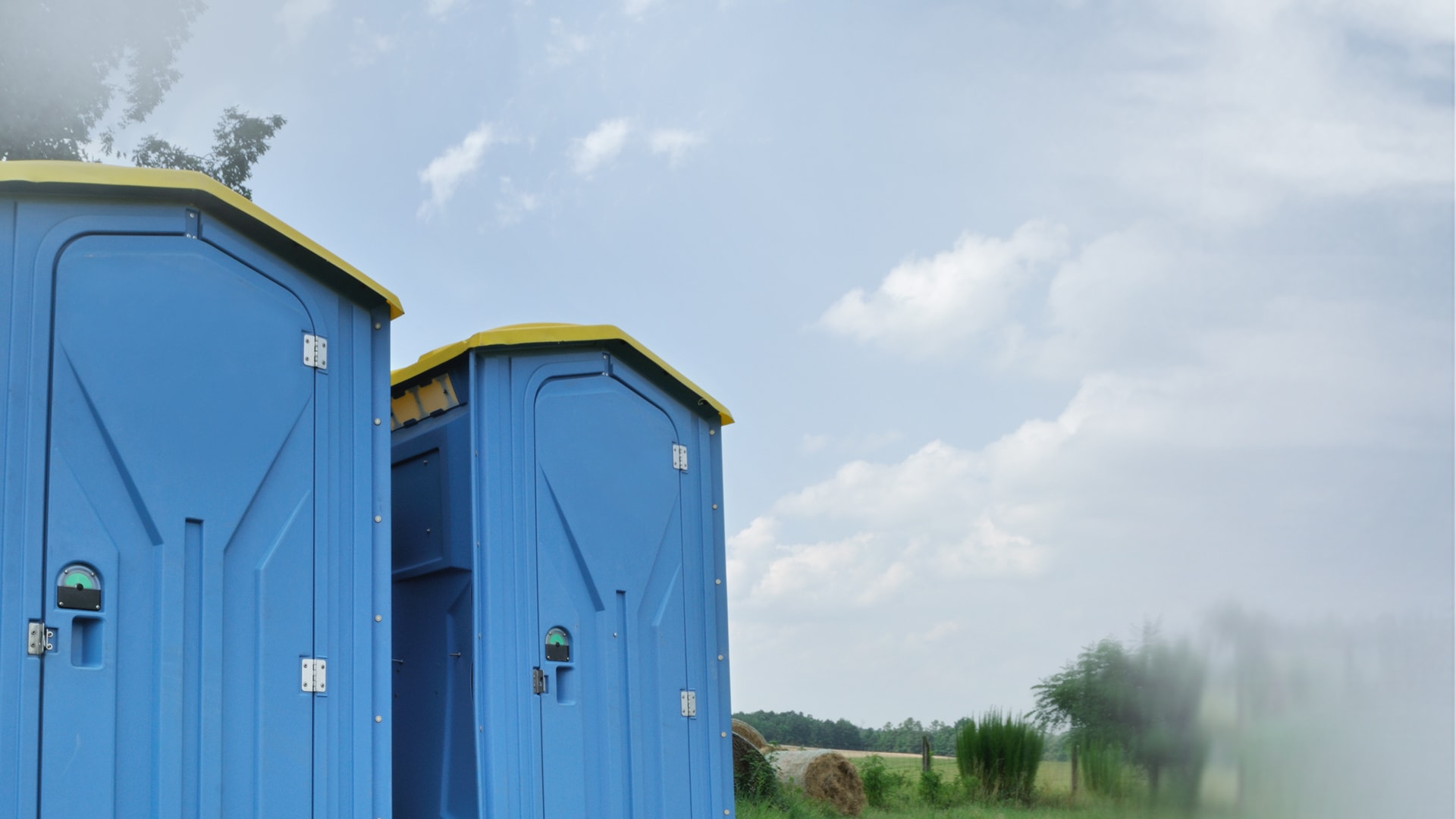Two blue thermoformed portable restrooms in a field
