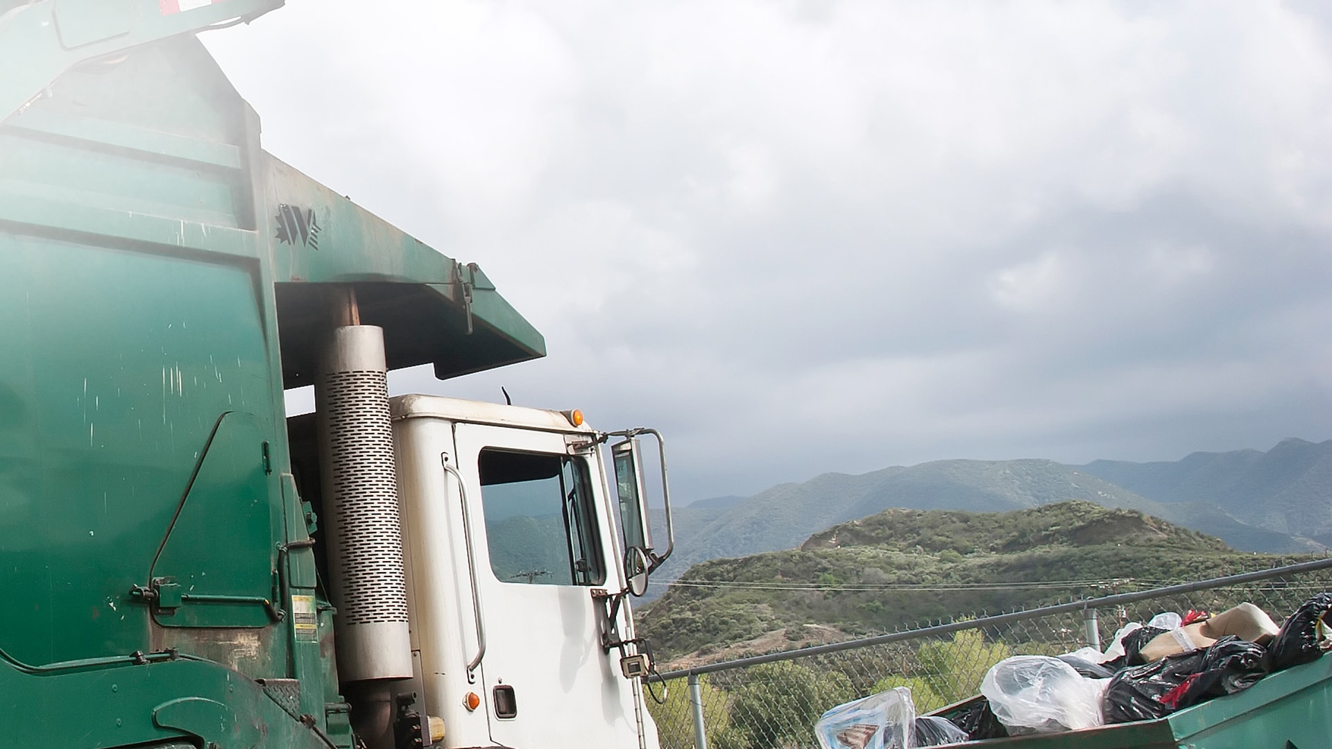 A green waste-collection truck at a roadside container